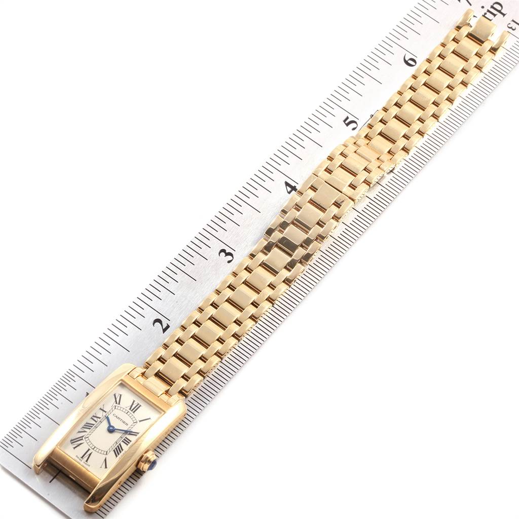 This image shows a Cartier Tank Americaine W26015K2 Women's Yellow Gold Silver Dial W26015K2 Women's Yellow Gold Silver Dial watch placed next to a ruler from an angled top view.