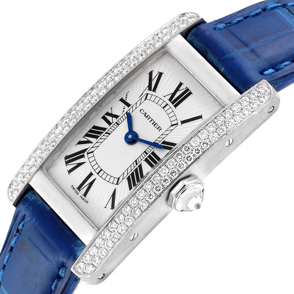 The image shows a Cartier Tank Américaine watch at an angled close-up, highlighting its face, diamond-studded case, and blue leather strap.