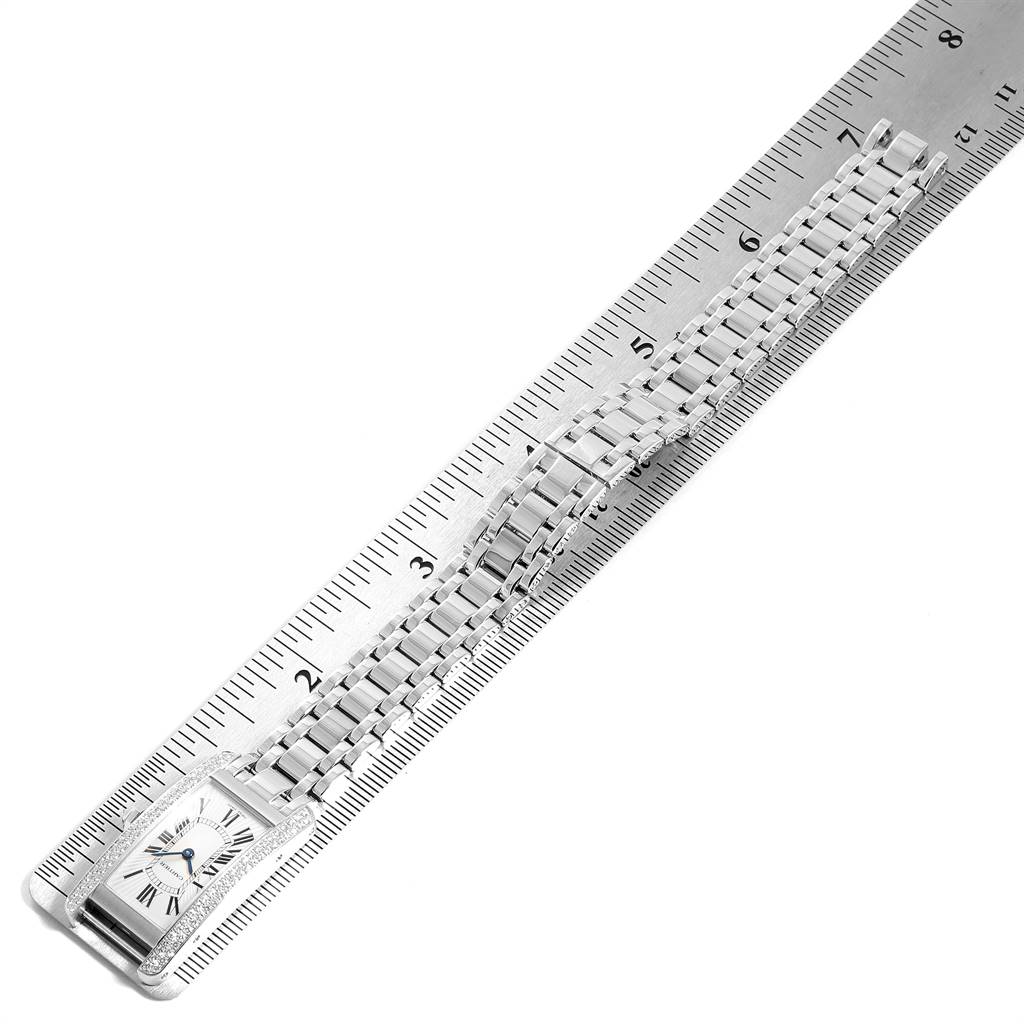 The image shows a top view of the Cartier Tank Americaine WB7018L1 Women's White Gold Silver Dial WB7018L1 Women's White Gold Silver Dial watch, displaying its case, bracelet, and clasp, placed alongside a ruler.