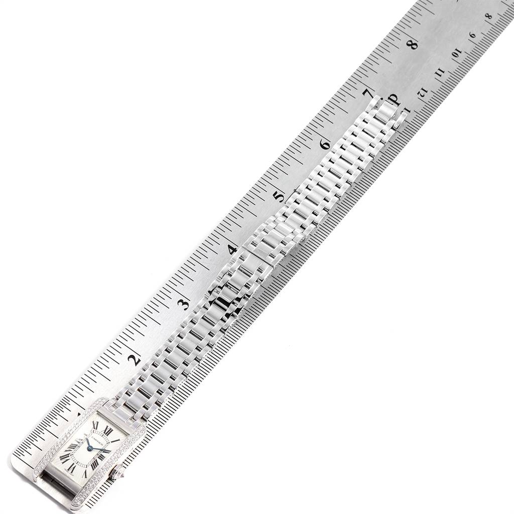 The Cartier Tank Americaine WB7018L1 Women's White Gold Silver Dial WB7018L1 Women's White Gold Silver Dial watch is shown from above, highlighting its face, metal bracelet, and part of a metal ruler for scale.