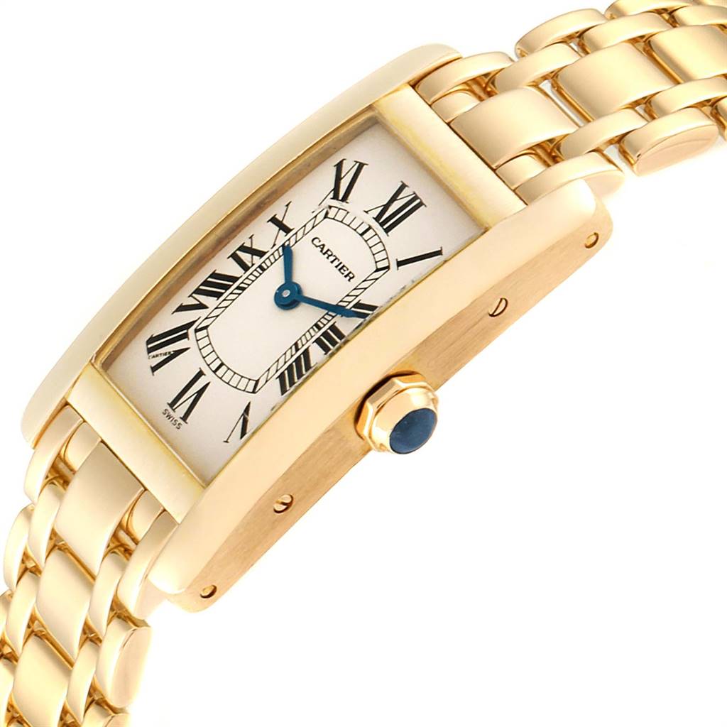 The Cartier Tank Americaine W26015K2 Women
s Yellow Gold Silver Dial W26015K2 Women
s Yellow Gold Silver Dial watch is depicted at an angled view, showcasing its gold case, blue crown, and Roman numeral dial.
