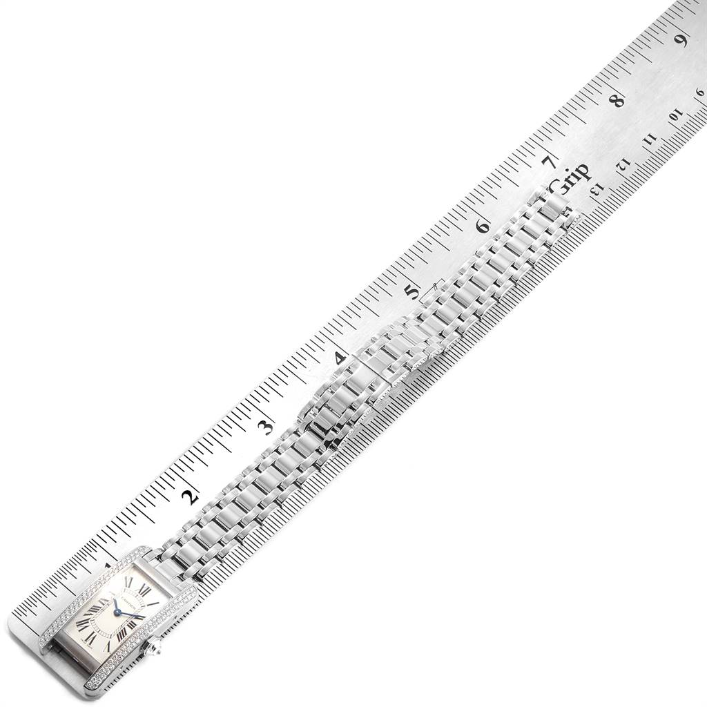 This image shows a top-down view of a Cartier Tank Americaine WB7018L1 Women
s White Gold Silver Dial WB7018L1 Women
s White Gold Silver Dial watch with a metal bracelet against a ruler, highlighting its length.