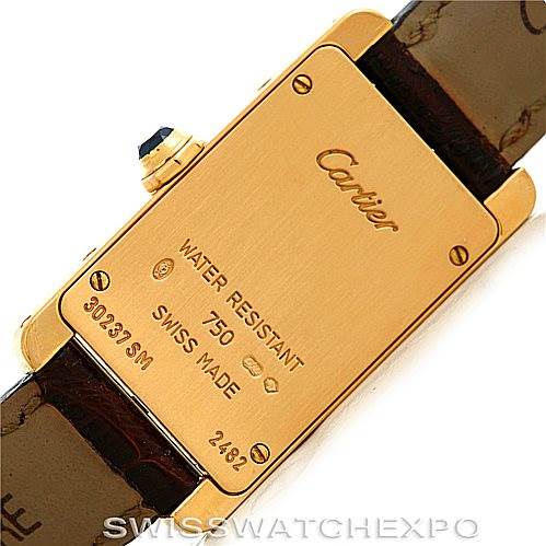 The image shows the back of a Tank Americaine model by Cartier, highlighting its inscriptions and leather strap attachments.