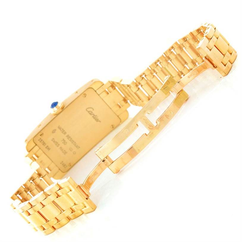 The image shows the backside of a Cartier Tank Americaine W26015K2 Women
s Yellow Gold Silver Dial W26015K2 Women
s Yellow Gold Silver Dial watch and its gold bracelet, including the clasp mechanism.
