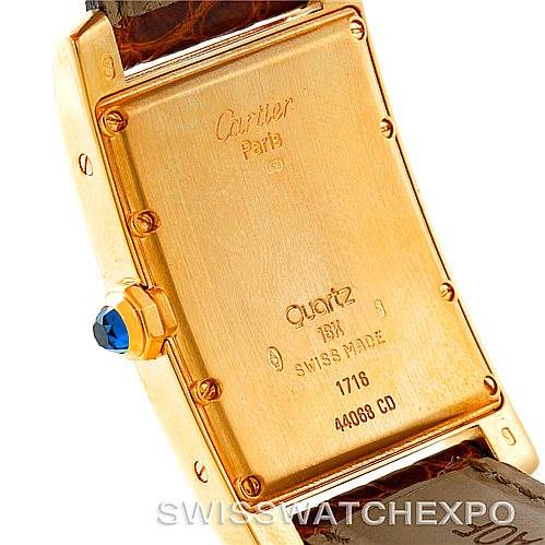 The image shows the back of the Tank Américaine model by Cartier, highlighting the case back, screws, and a winding crown with a blue gem.