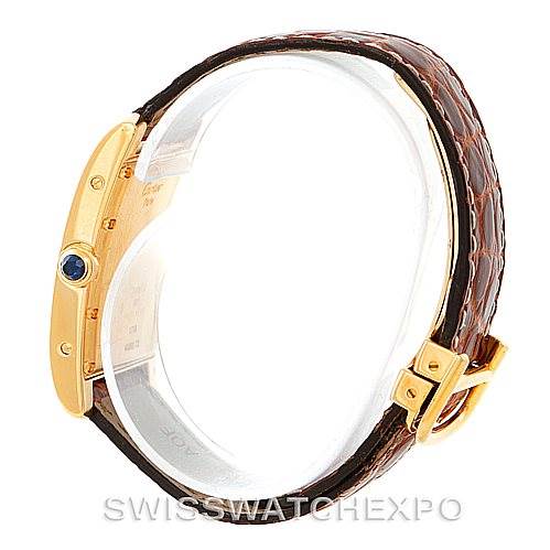 This image shows a side view of a Cartier Tank Américaine watch, highlighting its gold case, crown with a blue cabochon, and brown leather strap.