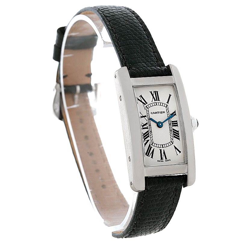 The image shows a Cartier Tank Americaine W2601956 Women
s White Gold Silver Dial W2601956 Women
s White Gold Silver Dial watch at a side angle, featuring its rectangular face, Roman numeral dial, and black leather strap.
