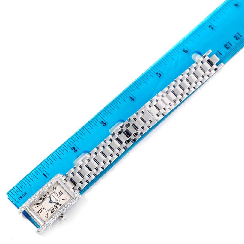 The Cartier Tank Americaine W2601956 Women
s White Gold Silver Dial W2601956 Women
s White Gold Silver Dial watch is shown from a top-down angle with its face, bezel, and strap alongside a blue ruler.