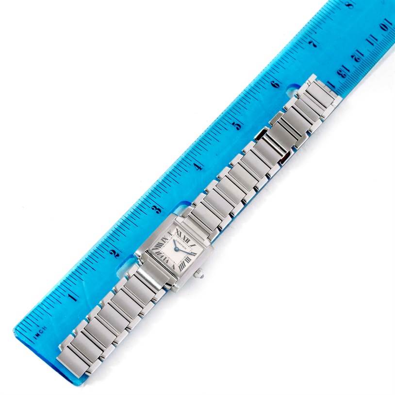 The image shows a Cartier Tank Française watch laid flat on a ruler, displaying the face and metal bracelet.