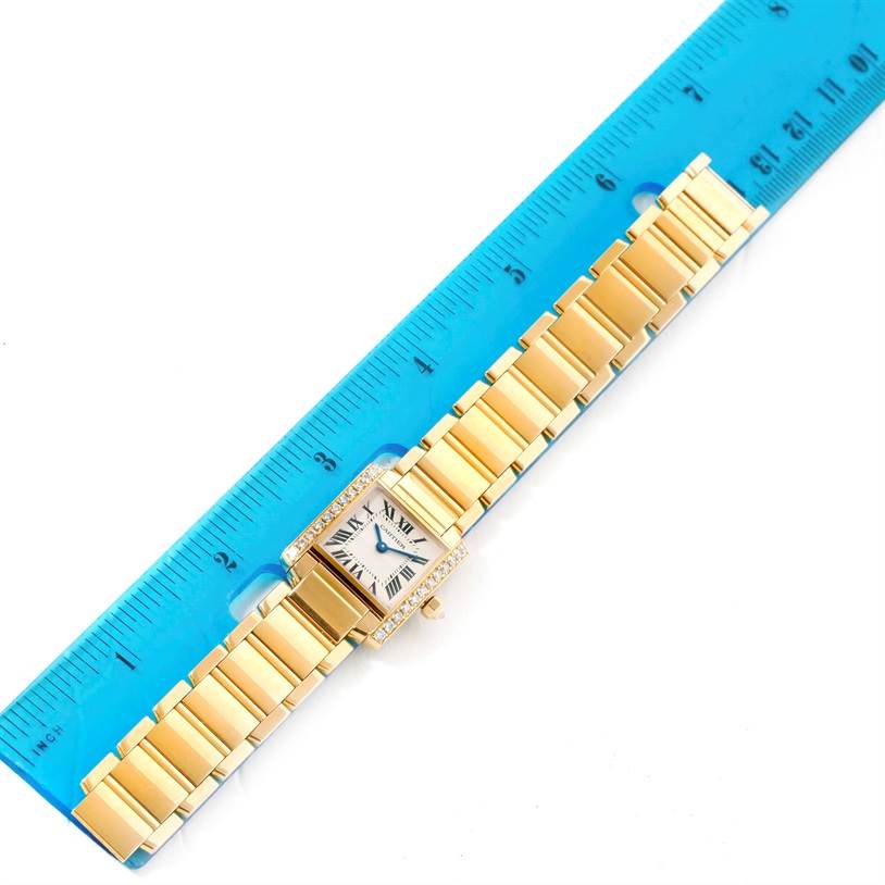 The image shows a top-down view of a Cartier Tank Française watch with a rectangular dial and a linked band next to a blue ruler.