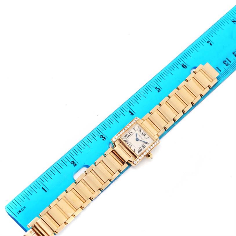 The image shows a top view of the Cartier Tank Francaise WE1001R8 Women's Yellow Gold Silver Dial WE1001R8 Women's Yellow Gold Silver Dial watch, including its strap next to a blue ruler for scale.
