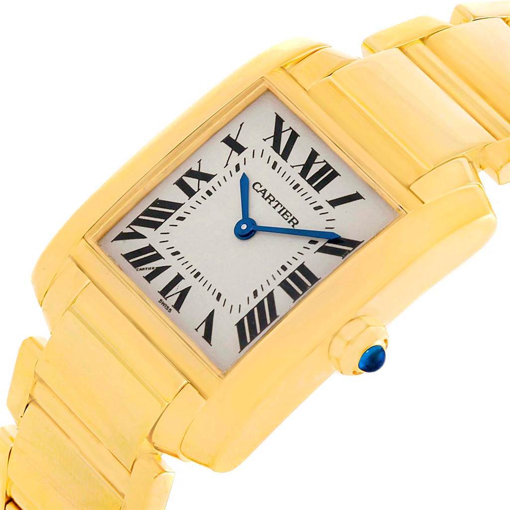 The image shows a close-up angle of a Cartier Tank Française watch, highlighting its gold case, bracelet, Roman numeral dial, and blue hands.