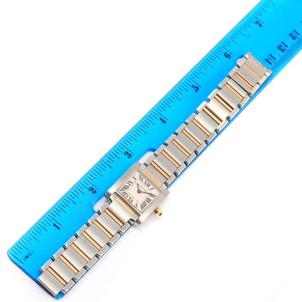 The image shows a Cartier Tank Française watch laid flat next to a blue ruler, showcasing its face and bracelet.