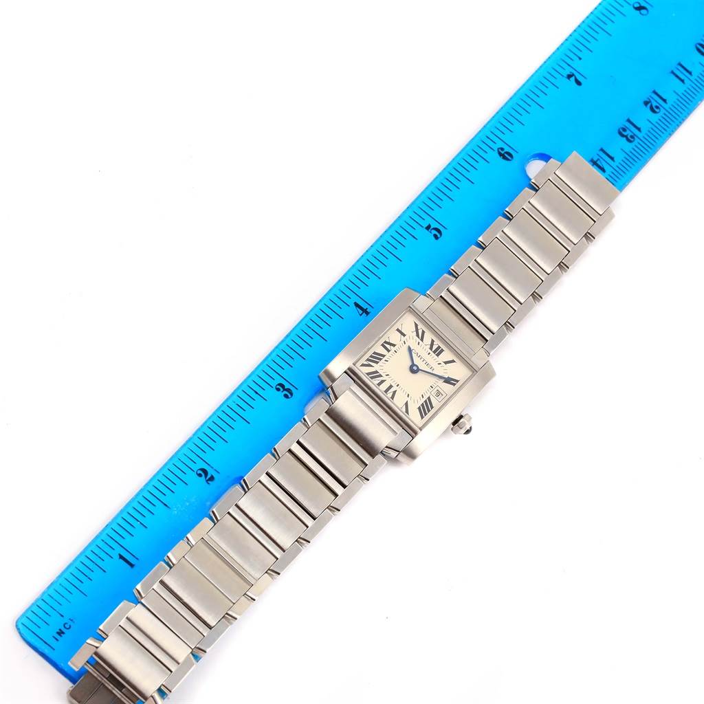 The image shows a Tank Française model by Cartier laid flat next to a blue ruler, displaying the watchband and face.