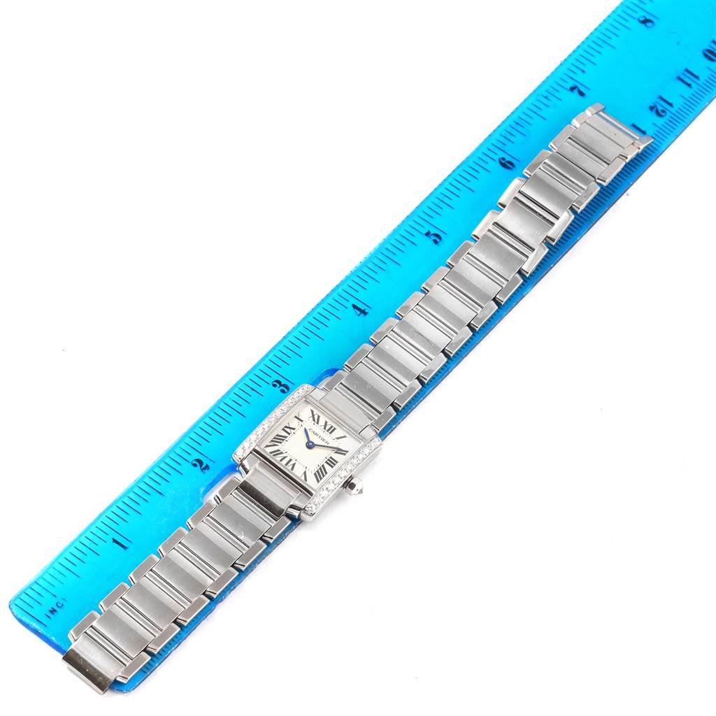 This image shows a top-down view of a Cartier Tank Francaise WE1002S3 Women's White Gold Silver Dial WE1002S3 Women's White Gold Silver Dial watch next to a blue ruler, highlighting its bracelet and face.