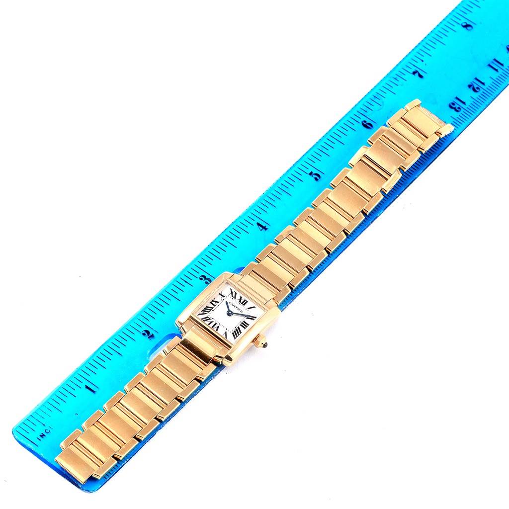 The Cartier Tank Francaise W50002N2 Women's Yellow Gold Silver Dial W50002N2 Women's Yellow Gold Silver Dial watch is shown flat, with its gold bracelet extended alongside a blue ruler.