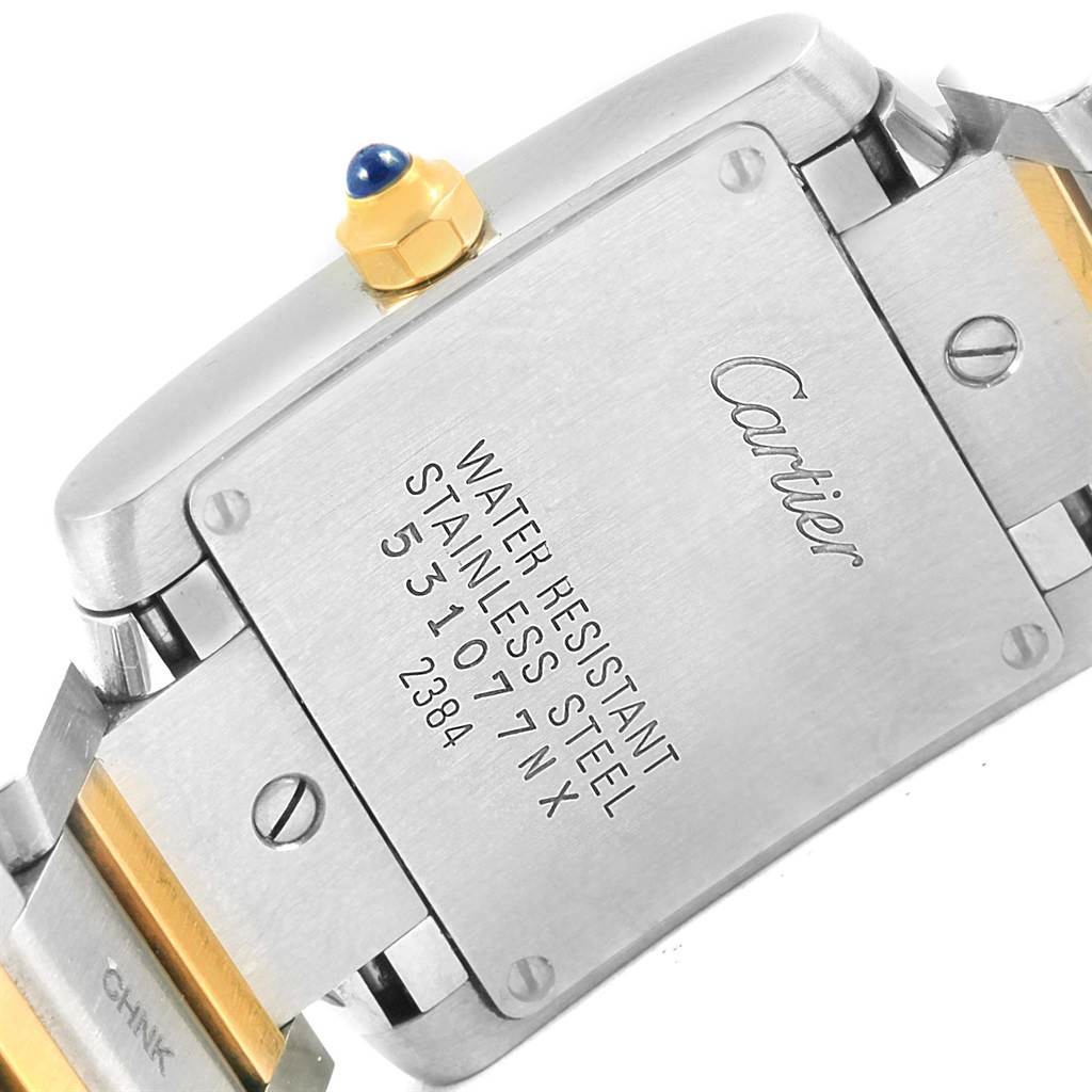 The image shows the backplate and crown of a Cartier Tank Française watch with visible screws and inscriptions.