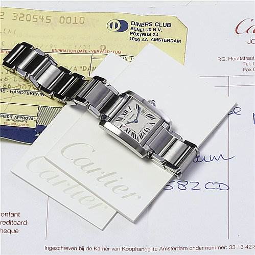 The Cartier Tank Francaise W51011Q3 Women's Stainless Steel Silver Dial W51011Q3 Women's Stainless Steel Silver Dial watch is shown from a top view, displaying its bracelet, face, and clasp and is placed on documentation and a card.