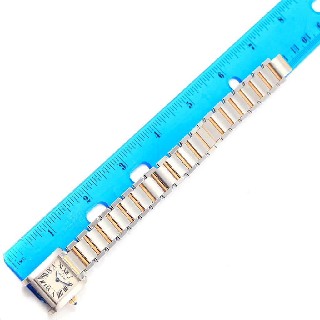 The image shows a Cartier Tank Française watch laid flat next to a blue ruler, displaying the watch face and band.