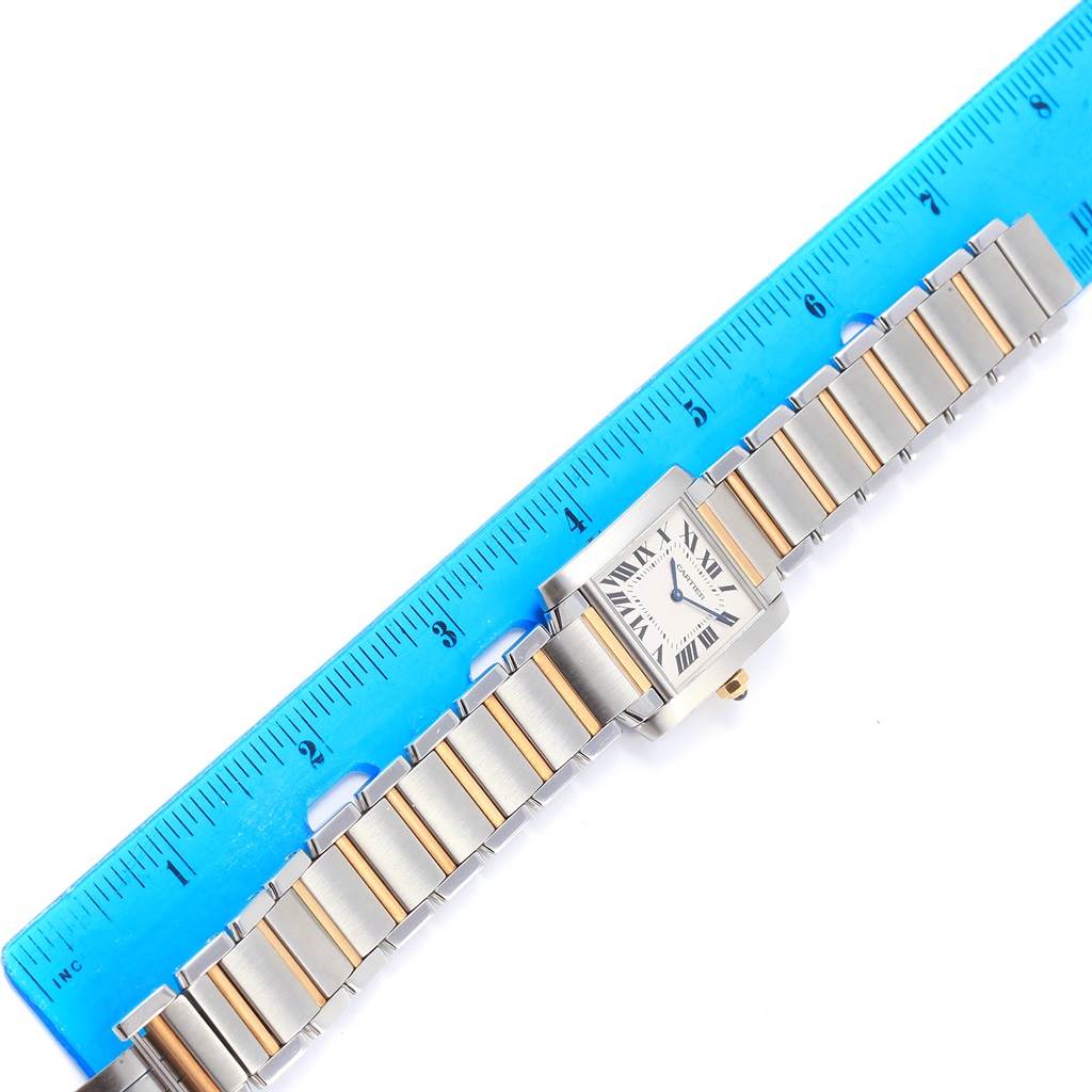 The image shows the Cartier Tank Francaise W2TA0003 Women's Steel and Gold (two tone) Silver Dial W2TA0003 Women's Steel and Gold (two tone) Silver Dial watch laid flat next to a ruler, displaying its face and metal bracelet.