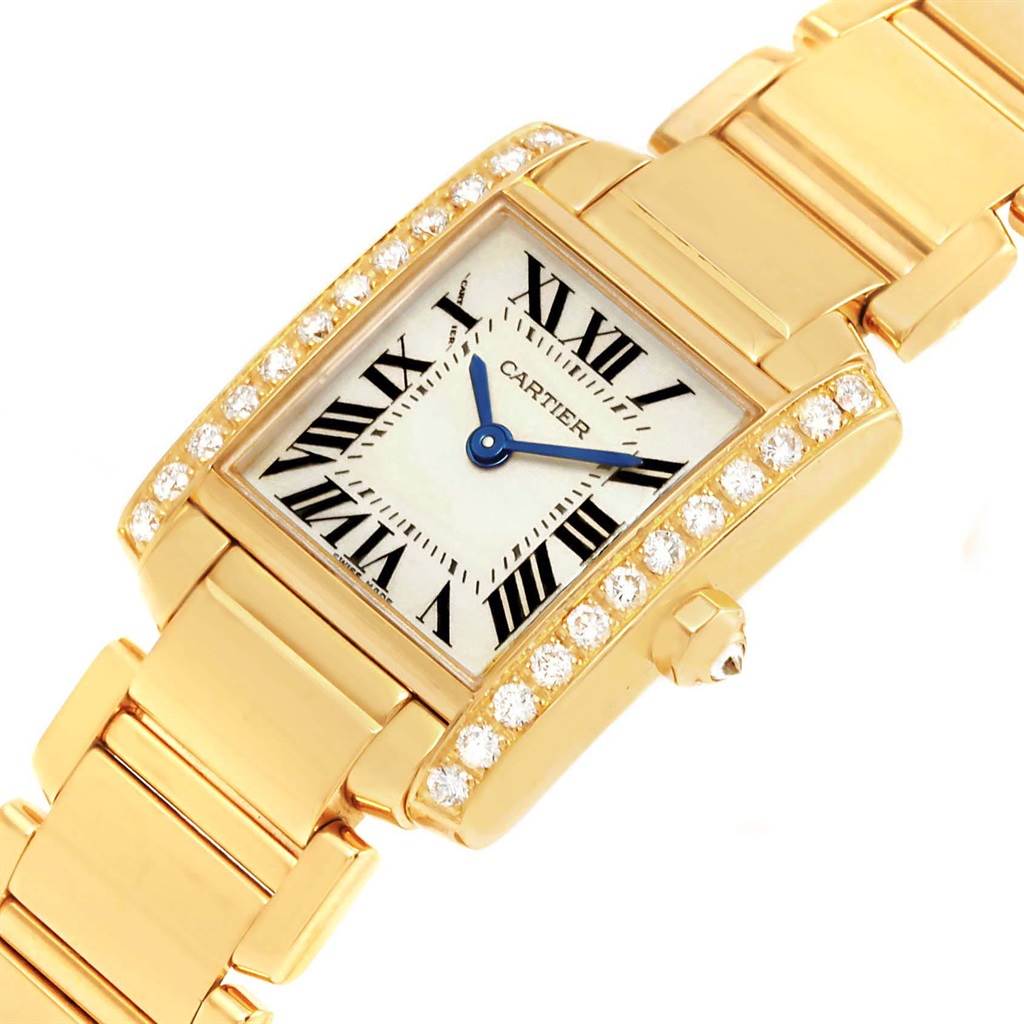 The image shows a close-up view of the Cartier Tank Francaise WE1001R8 Women's Yellow Gold Silver Dial WE1001R8 Women's Yellow Gold Silver Dial watch, highlighting its gold bracelet, rectangular face, and diamond-studded bezel.