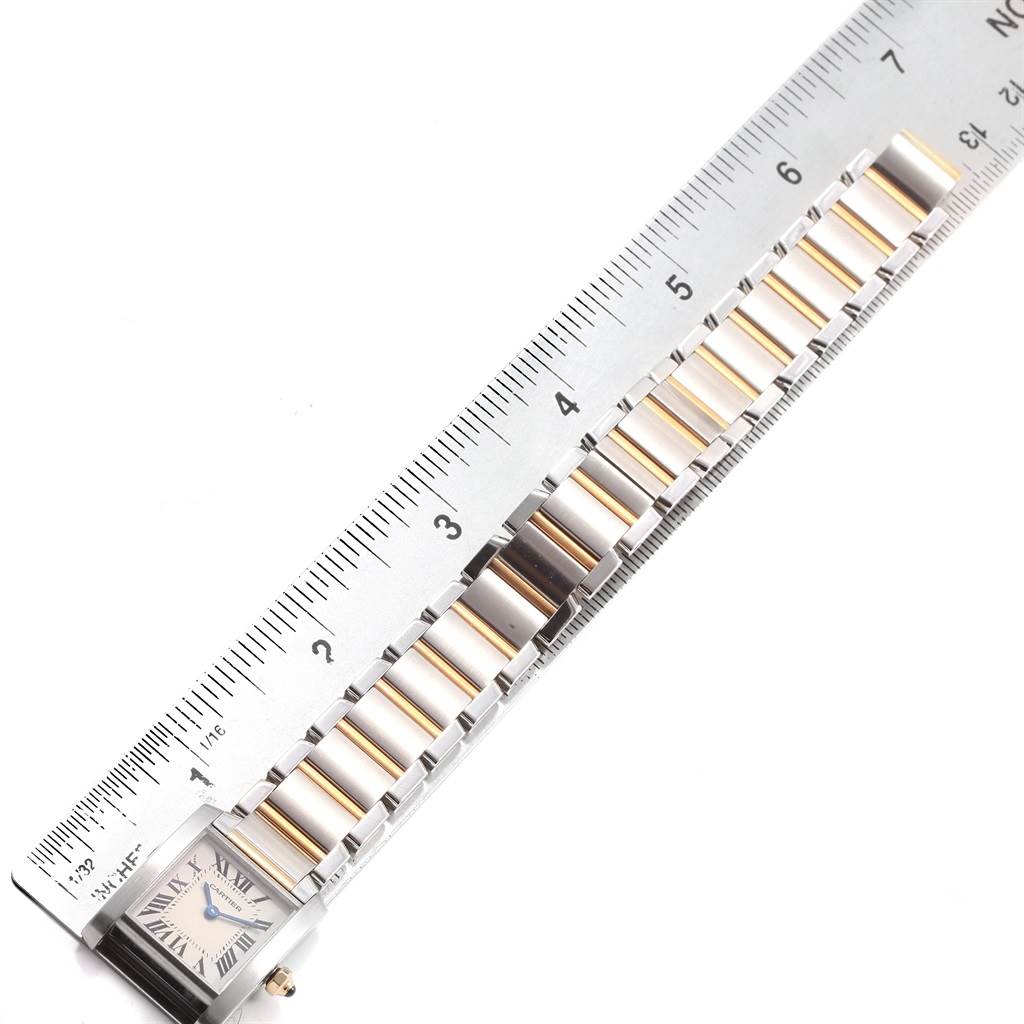 The image shows a Tank Française model by Cartier, featuring the watch case and bracelet next to a measuring ruler.