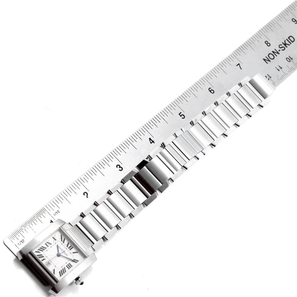 The image shows the Cartier Tank Française watch laid flat along a ruler, highlighting its length and metal bracelet.