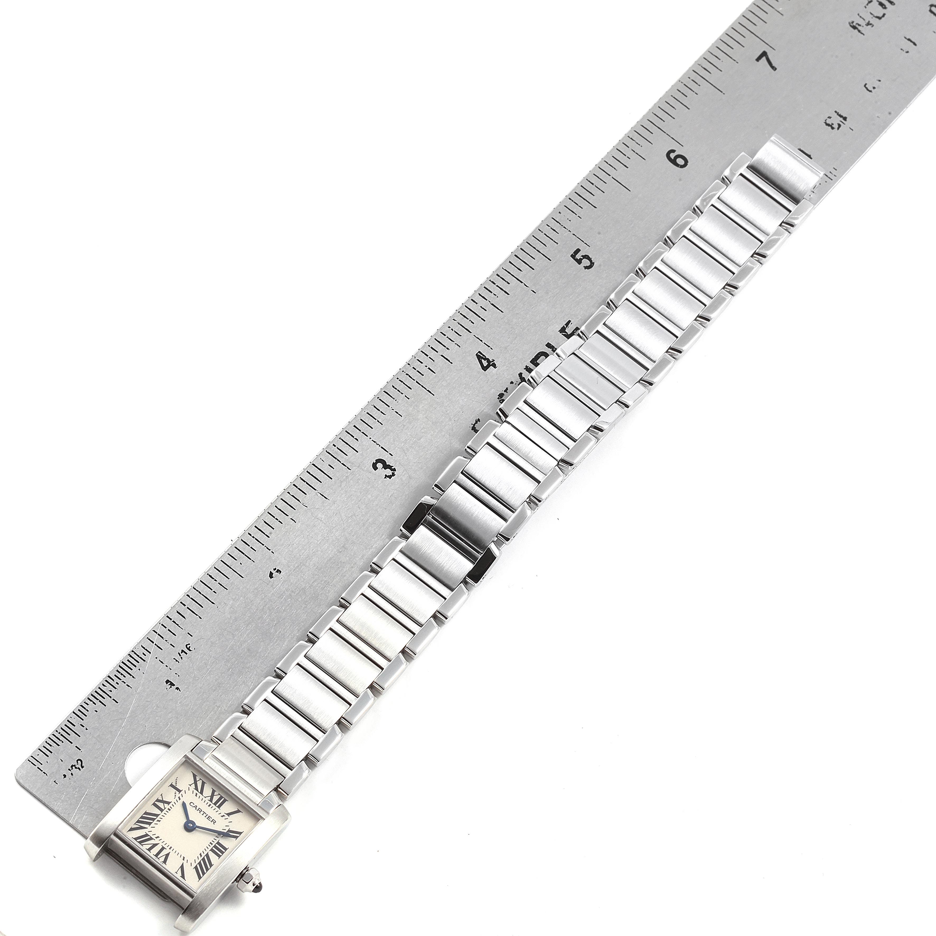 The Tank Francaise by Cartier is shown from above, displaying the face and the full length of the bracelet next to a ruler.