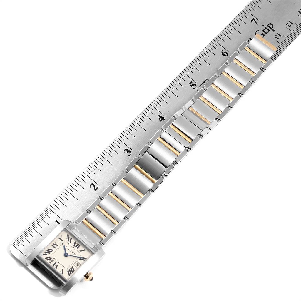 The image shows a Tank Francaise by Cartier laid flat against a ruler, displaying its watch face and part of the metal band.