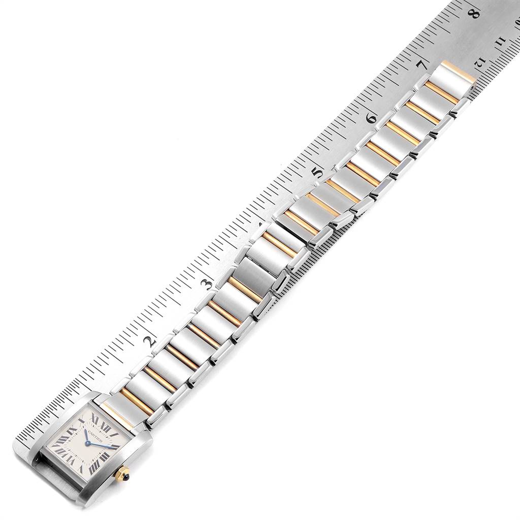 The image shows an overhead view of a Cartier Tank Française watch, highlighting its face and a part of the metal bracelet with gold accents, measured against a ruler.