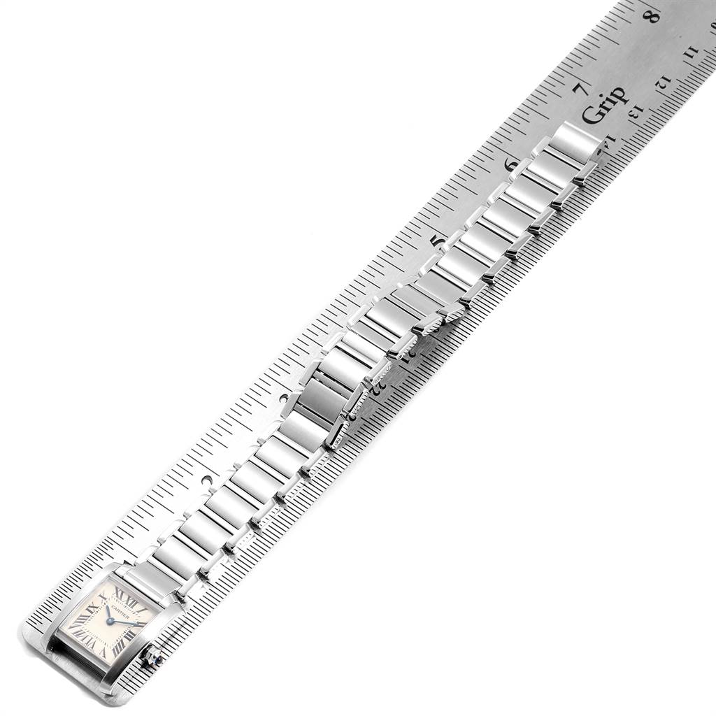 The Tank Francaise by Cartier is shown at an overhead angle, displaying its face and metal bracelet aligned with a ruler.