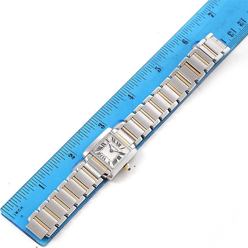 The image shows a top-down view of a Cartier Tank Française watch with its bracelet laid out next to a blue ruler.