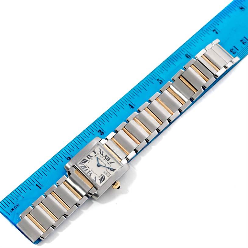 This image shows a Cartier Tank Française watch laid flat next to a blue ruler, displaying the face and bracelet.