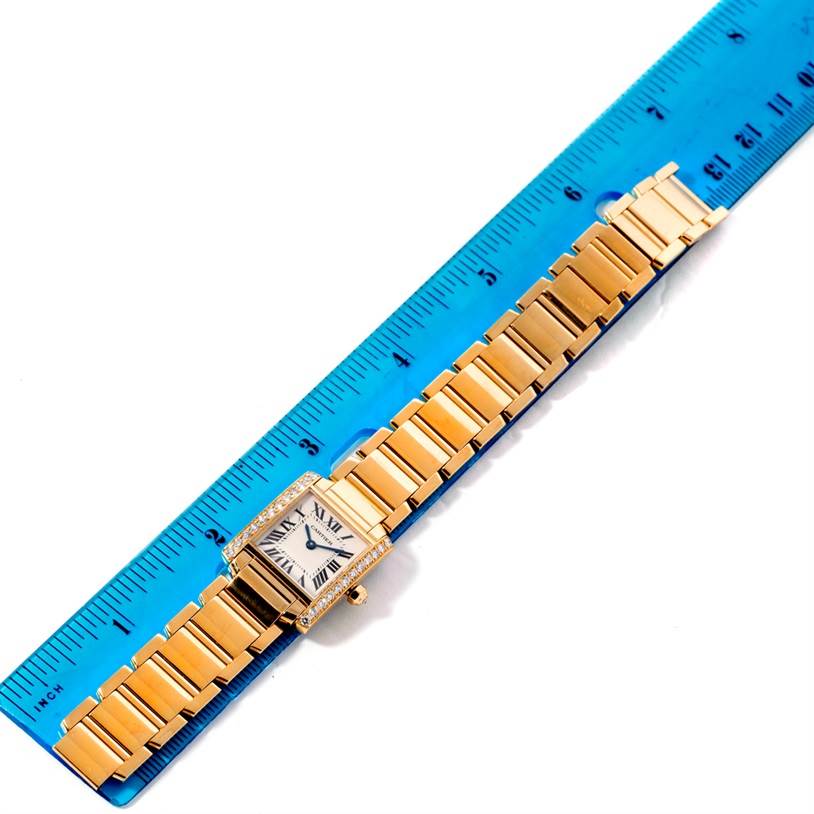 This image shows a Cartier Tank Francaise WE1001R8 Women's Yellow Gold Silver Dial WE1001R8 Women's Yellow Gold Silver Dial watch laid flat against a blue ruler, displaying its bracelet and face.