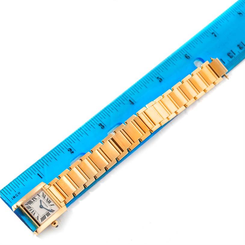 The image shows a Cartier Tank Française watch placed beside a blue ruler, displaying the watch face and bracelet links.