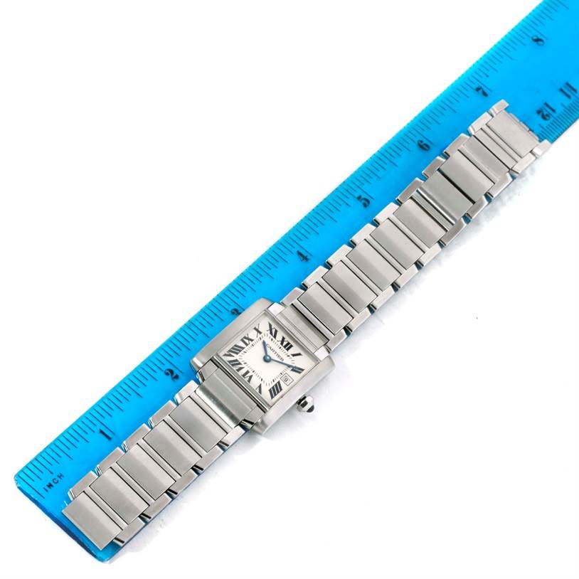 The Cartier Tank Française watch is shown flat against a blue ruler, displaying its face and metal bracelet.