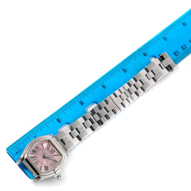 The image shows a Cartier Roadster W62017V3 Women's Stainless Steel Pink Dial W62017V3 Women's Stainless Steel Pink Dial watch placed next to a blue ruler, highlighting the watch face and metal bracelet.