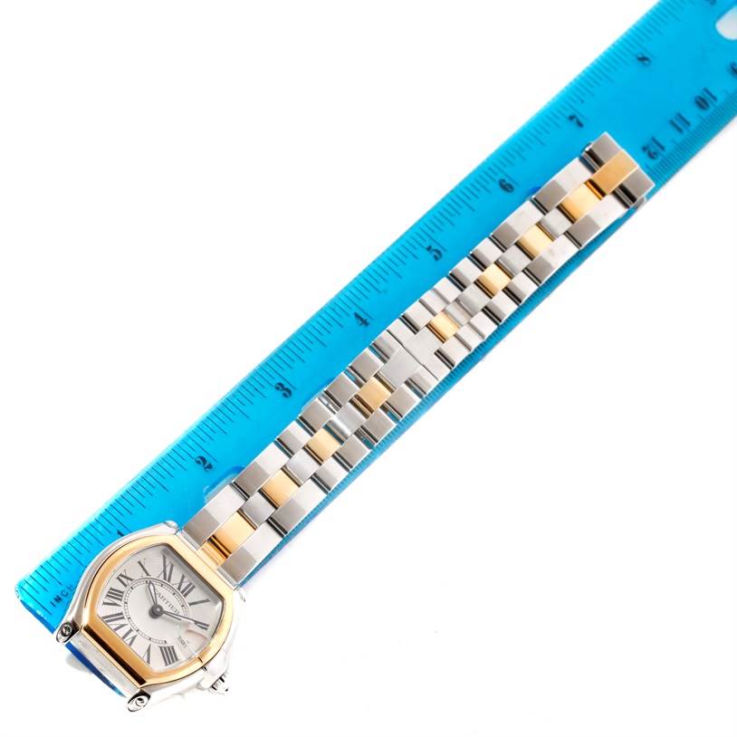 The image shows a Cartier Roadster W62026Y4 Women's Steel and Gold (two tone) Silver Dial W62026Y4 Women's Steel and Gold (two tone) Silver Dial watch placed alongside a blue ruler, highlighting the watch face and the metal strap.