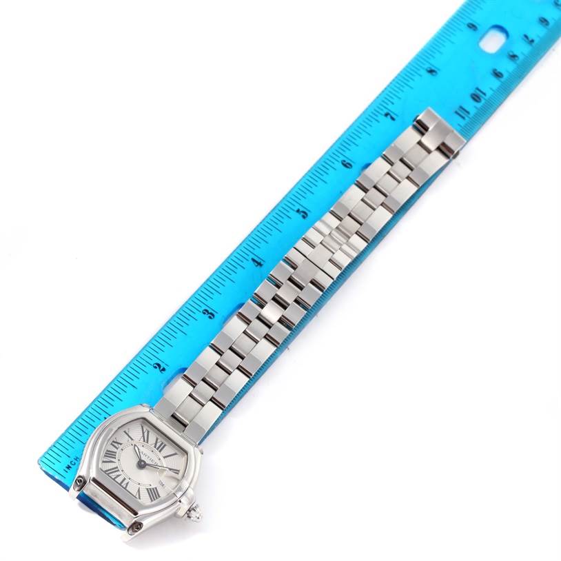The Cartier Roadster W62016V3 Women
s Stainless Steel Silver Dial W62016V3 Women
s Stainless Steel Silver Dial watch is shown at a top-down angle alongside a blue ruler for scale, displaying the face and metal bracelet.