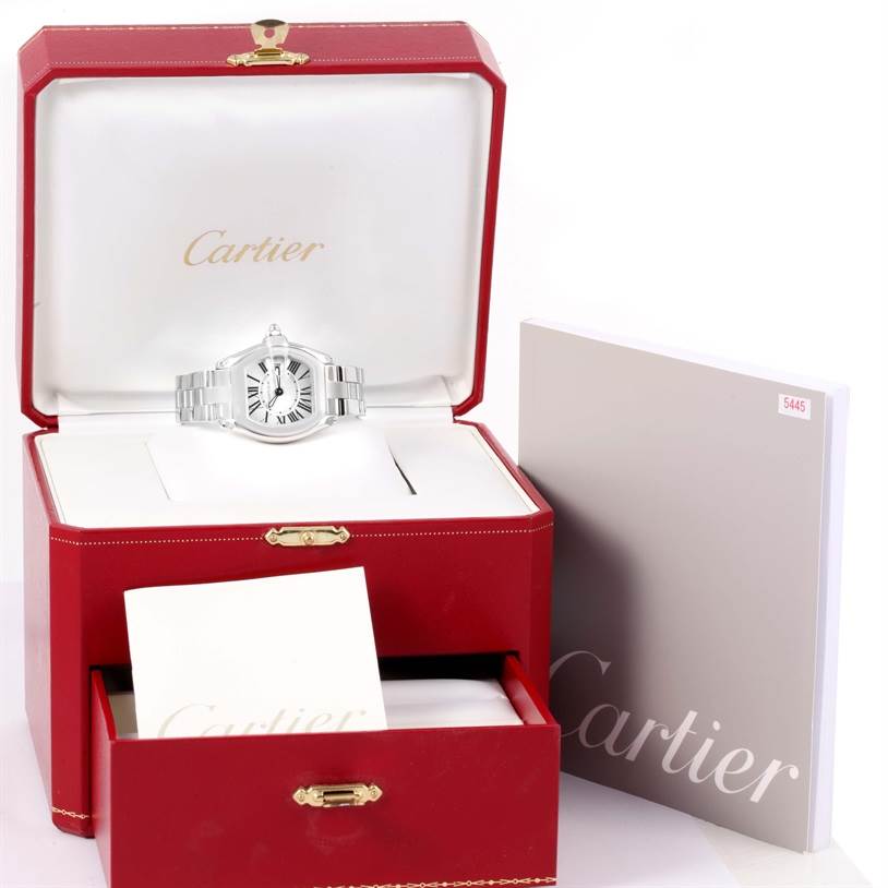 The image shows a Cartier Roadster W62016V3 Women
s Stainless Steel Silver Dial W62016V3 Women
s Stainless Steel Silver Dial watch in an open red box with additional booklets and papers.