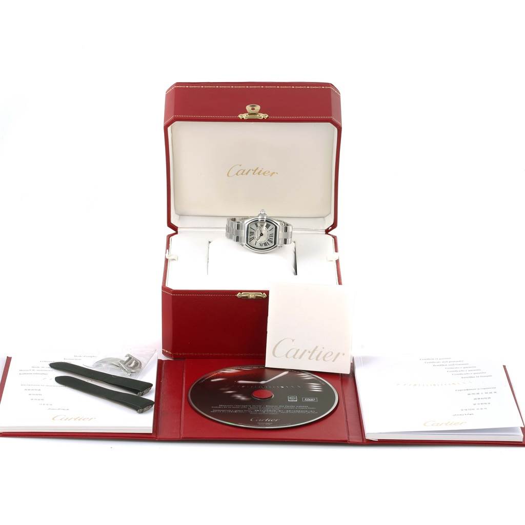 The Cartier Roadster W62016V3 Women
s Stainless Steel Silver Dial W62016V3 Women
s Stainless Steel Silver Dial watch is shown front-facing, displayed with its accessories including extra straps, a buckle, a CD, and documentation.
