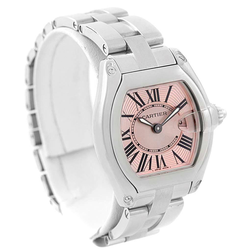 The Cartier Roadster W62017V3 Women's Stainless Steel Pink Dial W62017V3 Women's Stainless Steel Pink Dial watch is shown at a front-side angle, highlighting the pink dial, Roman numerals, and stainless steel bracelet.