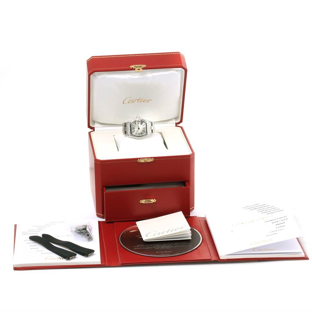 The Cartier Roadster W62016V3 Women
s Stainless Steel Silver Dial W62016V3 Women
s Stainless Steel Silver Dial watch is shown face-up in its packaging, along with additional straps, a booklet, and a CD.