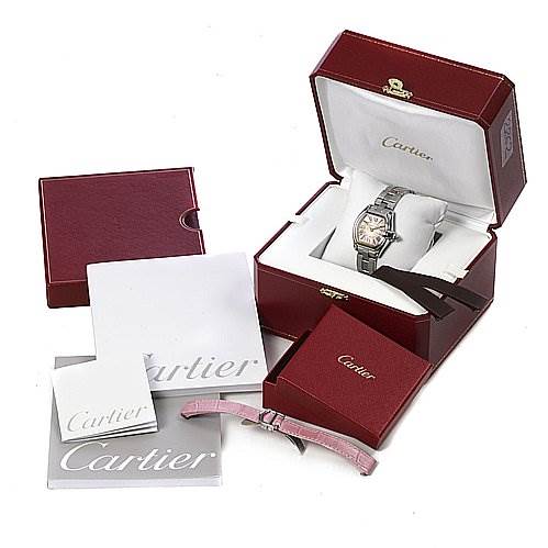 The image shows a Cartier Roadster W62017V3 Women
s Stainless Steel Pink Dial W62017V3 Women
s Stainless Steel Pink Dial watch in its box, with additional accessories including booklets and a pink strap, from a slightly top-down angle.