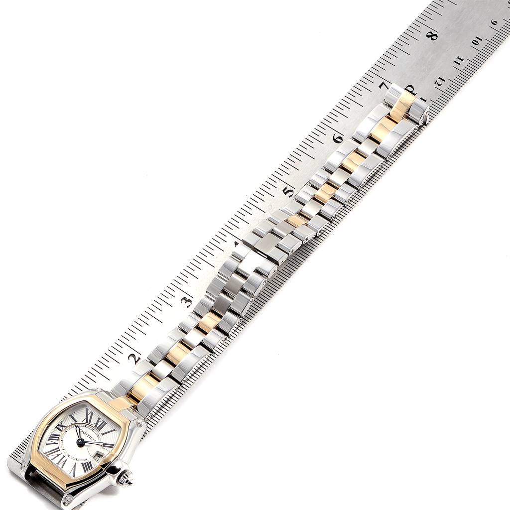 The Cartier Roadster W62026Y4 Women's Steel and Gold (two tone) Silver Dial W62026Y4 Women's Steel and Gold (two tone) Silver Dial watch is shown from an overhead angle, displaying its face, bezel, and metal bracelet next to a ruler.