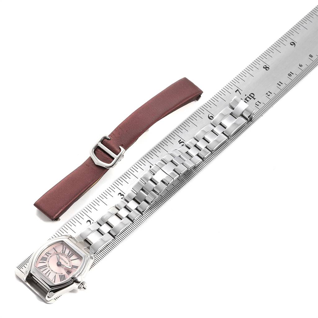 This image shows a Cartier Roadster W62017V3 Women's Stainless Steel Pink Dial W62017V3 Women's Stainless Steel Pink Dial watch and an additional leather watch strap placed beside a ruler for scale.