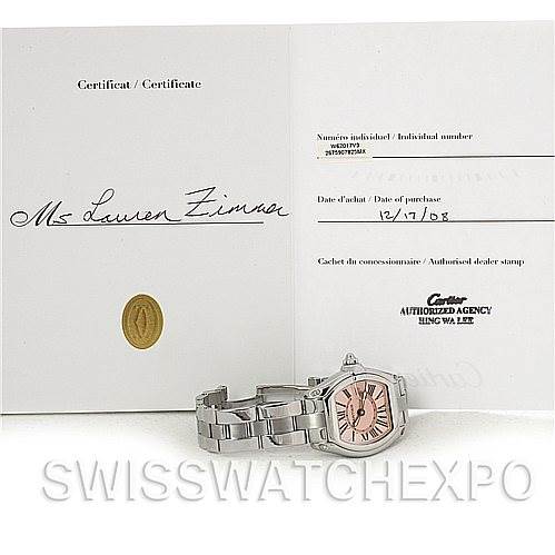 The image shows a Cartier Roadster W62017V3 Women's Stainless Steel Pink Dial W62017V3 Women's Stainless Steel Pink Dial watch and its certification, photographed from a low angle.