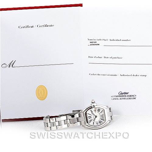 The image shows a Cartier Roadster W62016V3 Women's Stainless Steel Silver Dial W62016V3 Women's Stainless Steel Silver Dial watch lying flat with its certificate on display behind it.