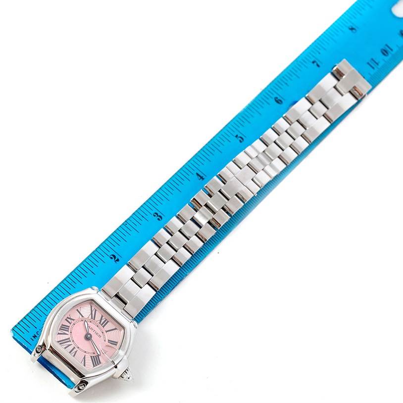 The Cartier Roadster W62017V3 Women's Stainless Steel Pink Dial W62017V3 Women's Stainless Steel Pink Dial watch is shown from a top-down angle, with a pink dial and metal bracelet positioned alongside a blue ruler.