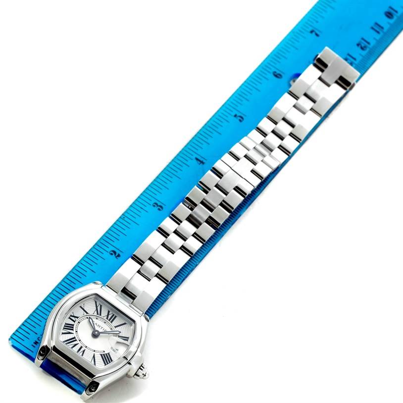 The Cartier Roadster W62016V3 Women's Stainless Steel Silver Dial W62016V3 Women's Stainless Steel Silver Dial watch is shown from a top-down angle, displaying the face and full metal bracelet on a blue ruler.